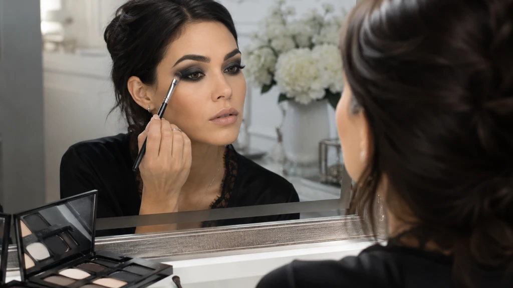 Femme réalisant un maquillage yeux noir smoky eyes devant un miroir avec un pinceau estompeur.