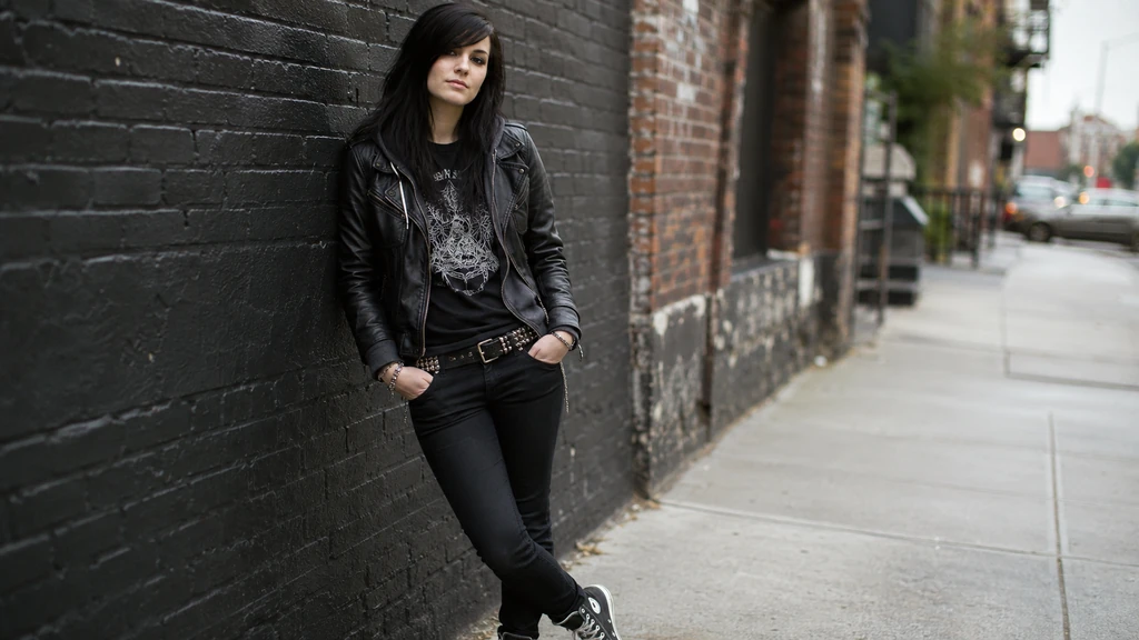 Jeune femme au style emo portant veste en cuir, jean noir skinny et t-shirt graphique dans une rue urbaine