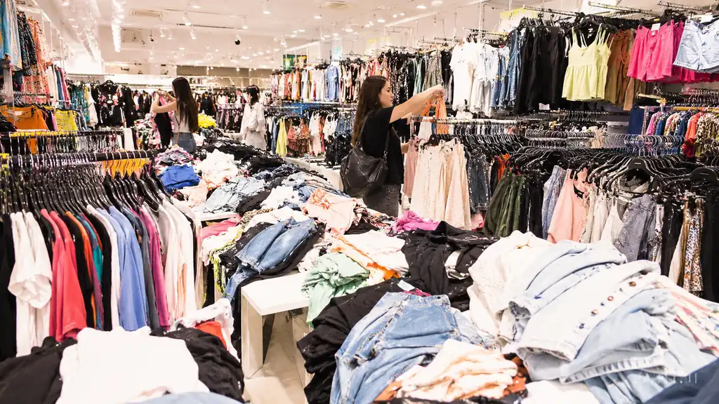 Cliente dans un magasin rempli de vêtements illustrant la surconsommation liée à la fast fashion