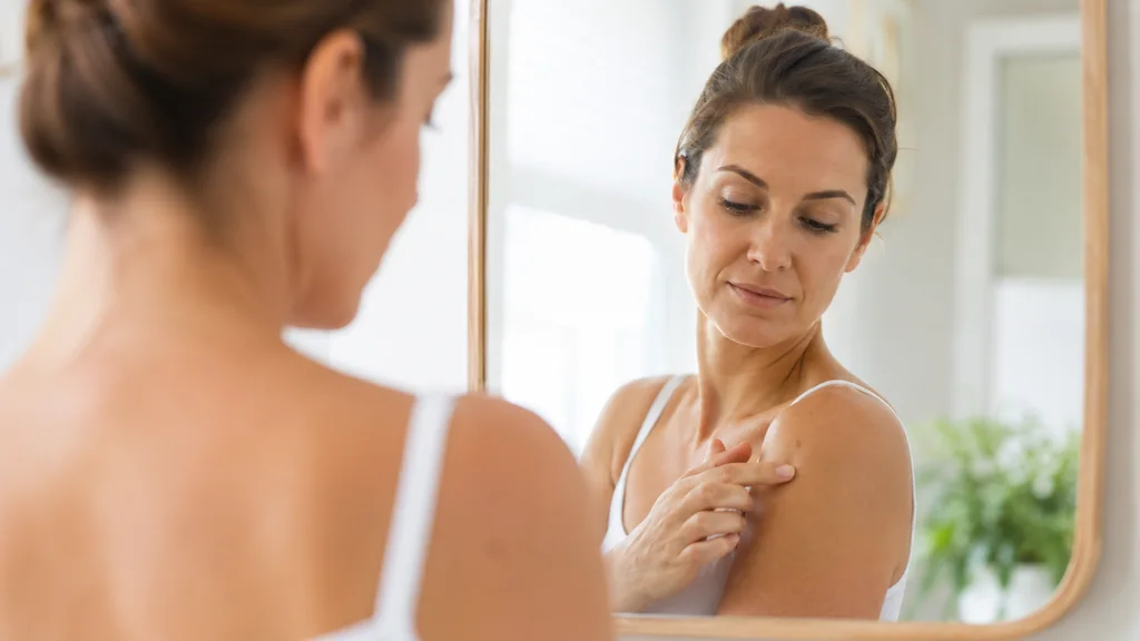 Femme observant un grain de beauté en relief sur son épaule devant un miroir lumineux
